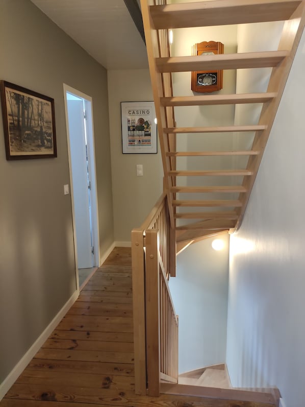 A wooden staircase with a handrail, a door at the bottom, and two framed pictures on the wall. - Charming little fisherman's cottage with a garden, 5 minutes from the beach (Port-Louis)