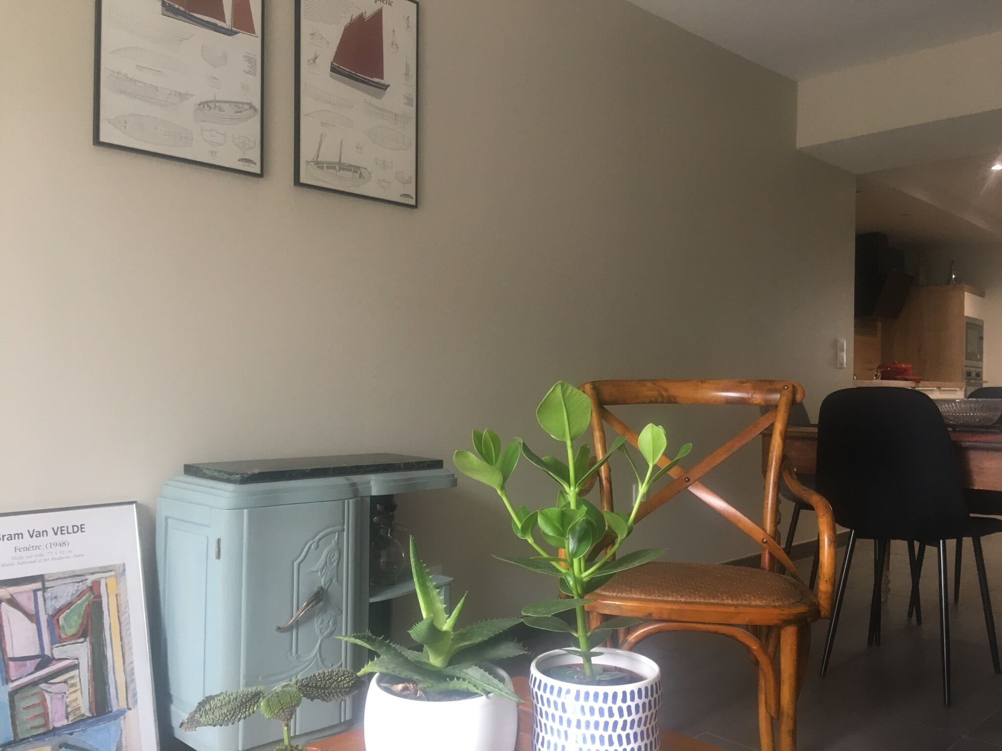 Une pièce comprenant un coin repas, une chaise en bois, une petite table avec une plante et un meuble contenant des œuvres d’art.