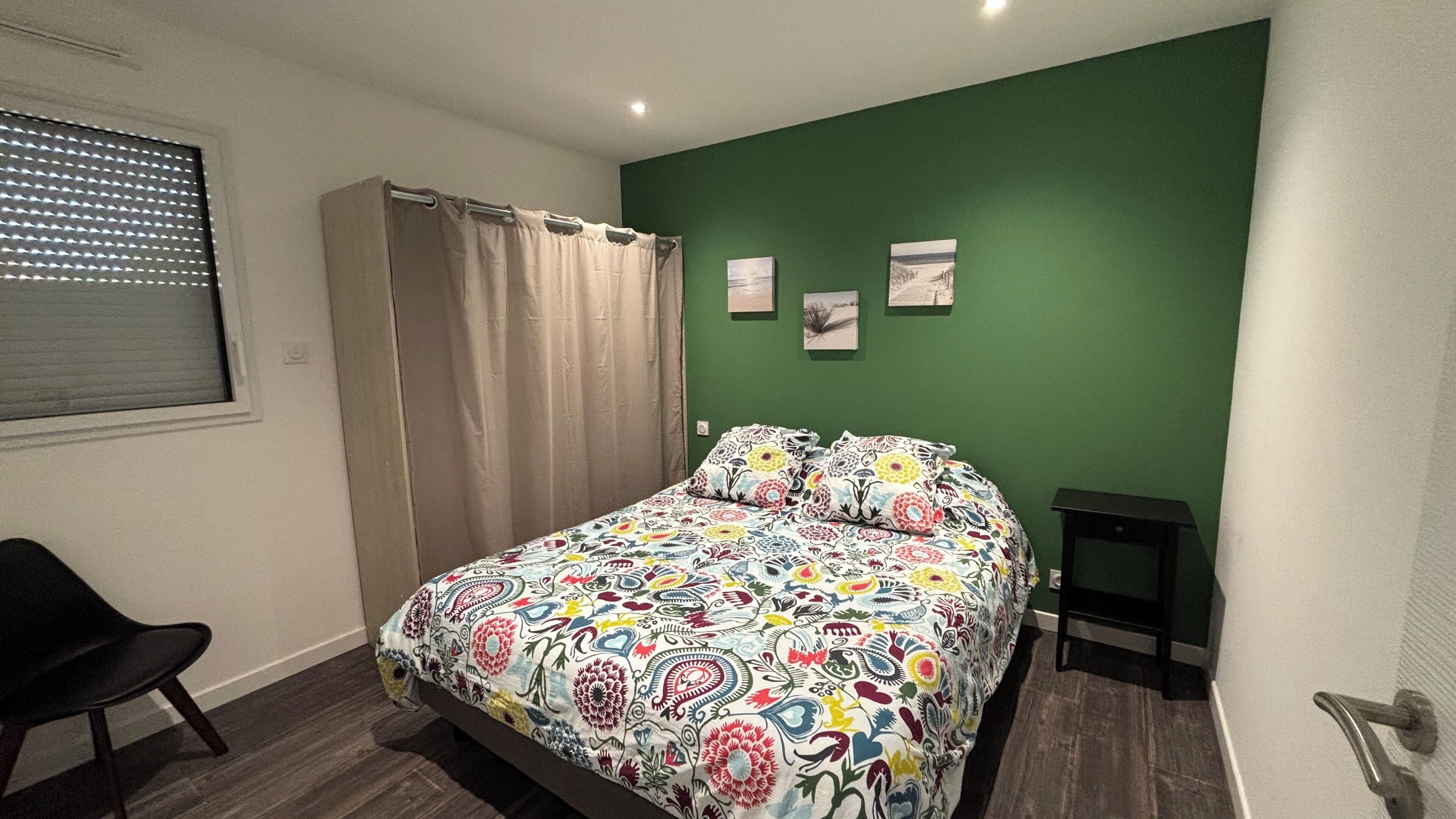 A bedroom with a bed, a chair, a small table, and a green wall.