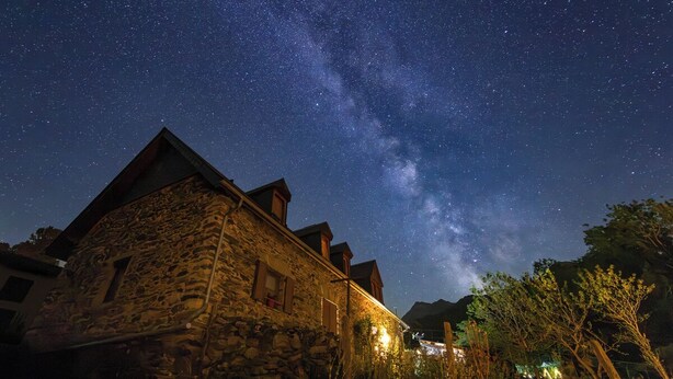 Un bâtiment en pierre doté d’un toit en pente, sous un ciel étoilé.