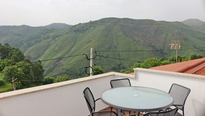 Un balcon doté d’une table ronde en verre et de quatre chaises, offrant une vue sur un paysage montagneux.