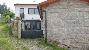 Un bâtiment en pierre avec une façade blanche et un toit rouge, agrémenté d’un portail noir et d’un petit espace porche.