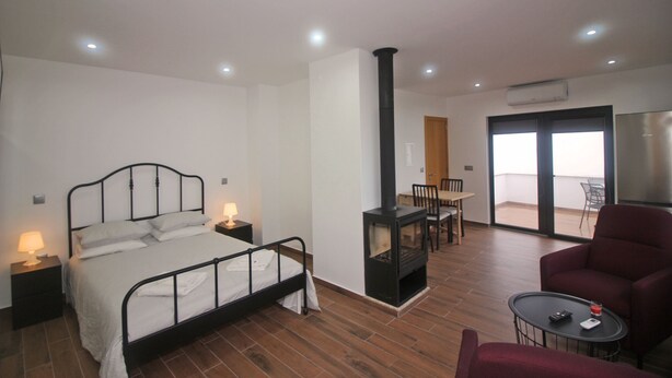 Une chambre à coucher avec un lit, des tables de chevet, une cheminée, un balcon avec une chaise et un fauteuil rouge.