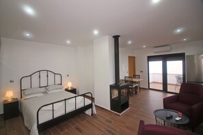A bedroom with a bed, bedside tables, a fireplace, a balcony with a chair, and a red armchair.
