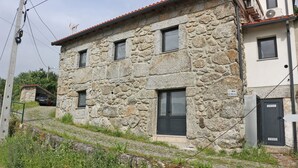 A stone building with a red-tiled roof, multiple windows, and a sign indicating 'RUA'. - House in Gerês for 2 people with fireplace (Gerês)