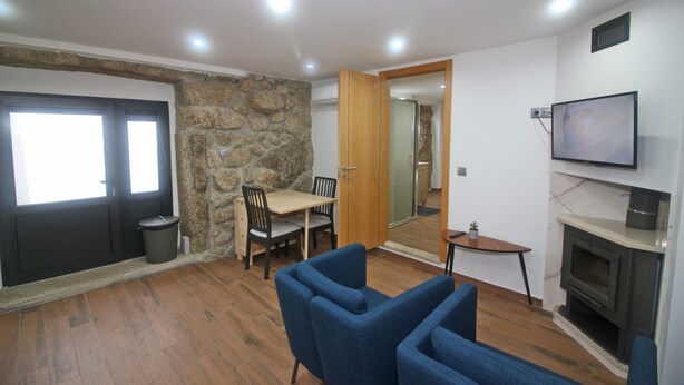 A living room with a stone wall, a fireplace, a TV, and a dining area with chairs and a table. - House in Gerês for 2 people with fireplace (Gerês)