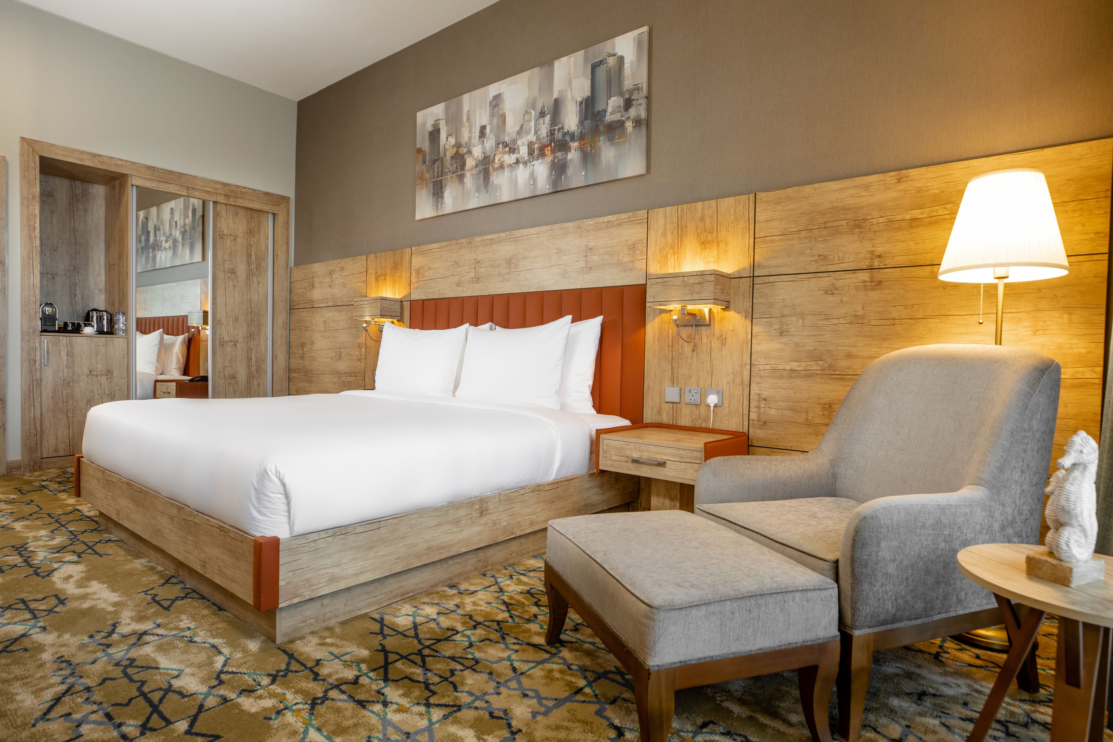 Een hotelkamer met een groot bed, een stoel, een klein tafeltje en een wandlamp.
