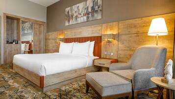 Een hotelkamer met een groot bed, een stoel, een klein tafeltje en een wandlamp.