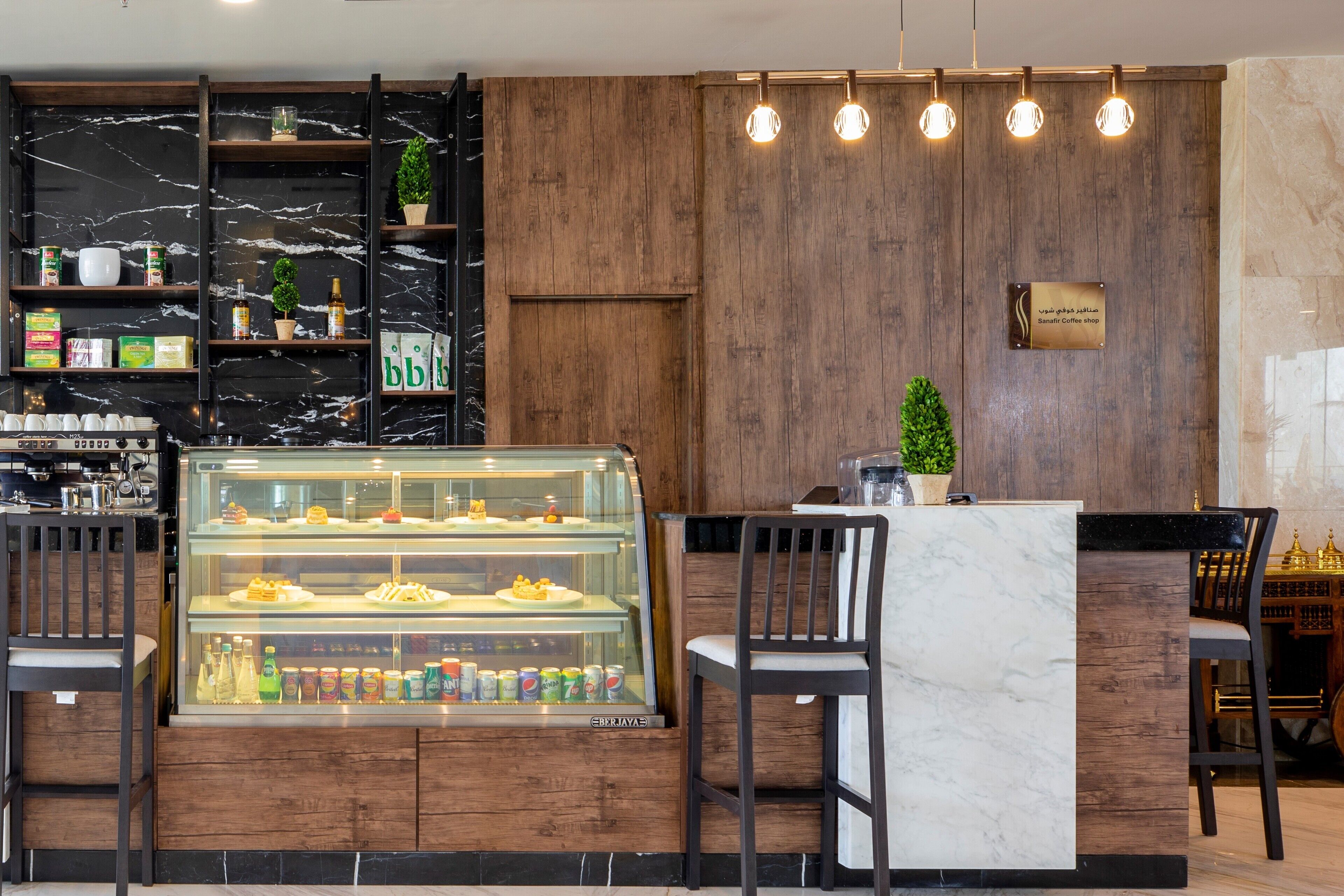 Un caffè moderno con banconi in marmo, una vetrina con pasticcini e scaffali in legno con snack e bevande.