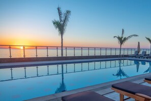 A poolside view with a sunset, palm trees, and lounge chairs. - Waves Hotel (Umluj)