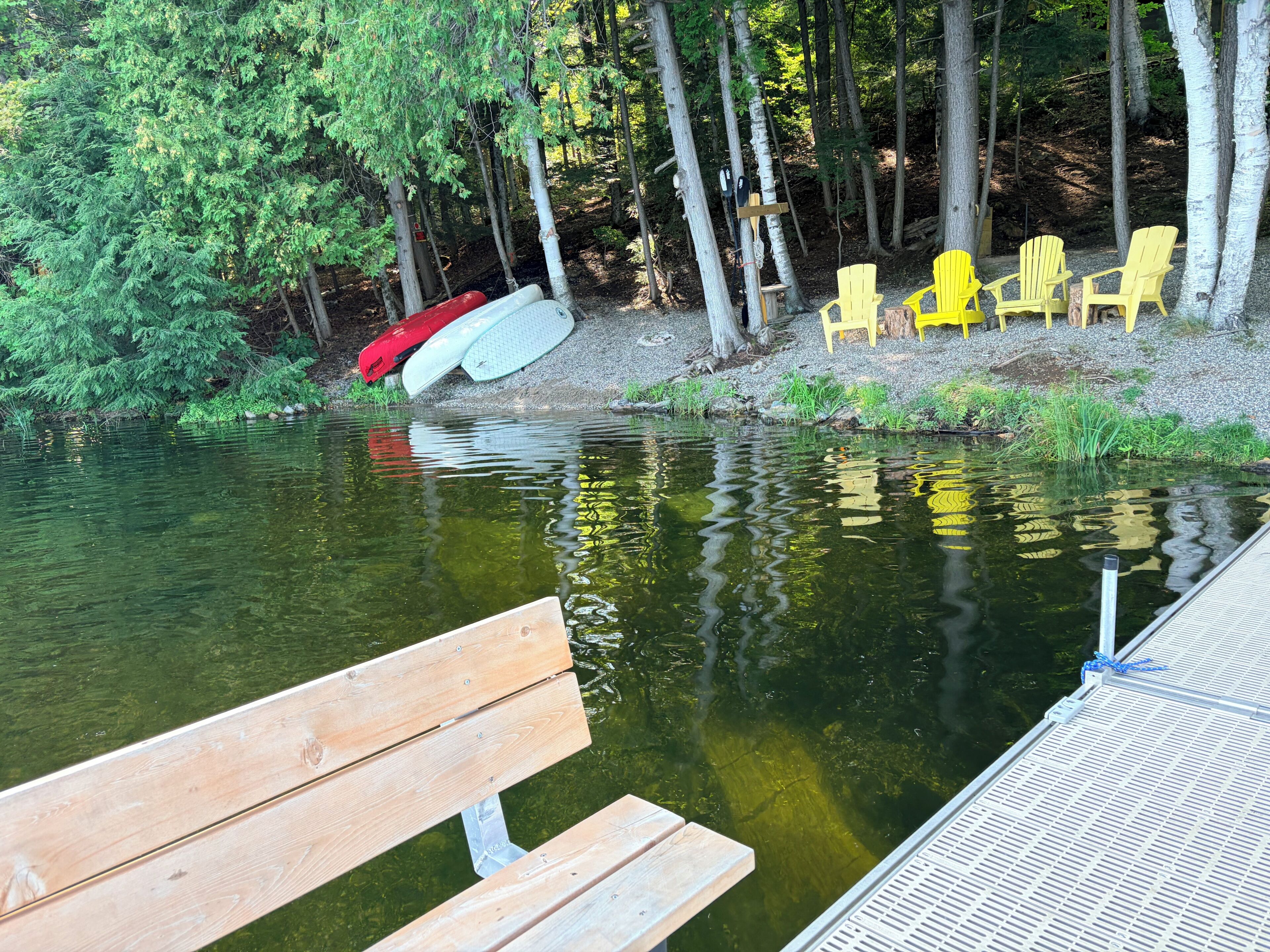 Une jetée en bois s’étendant sur une étendue d’eau, avec un banc et des chaises jaunes à proximité.