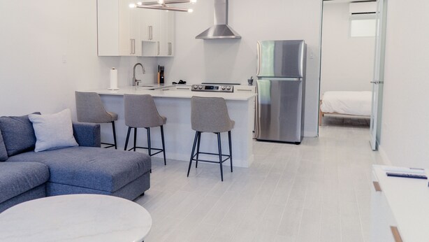A modern kitchen with a stainless steel refrigerator, a built-in oven, and a gas stove. There are four bar stools and a white dining table. - CENTRALLY-LOCATED CONDO (San Juan)