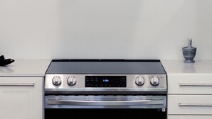 A kitchen with a stainless steel range hood, a digital oven control panel, and a small marble-like container. - CENTRALLY-LOCATED CONDO (San Juan)