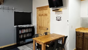 A compact living space with a dining area, a bookshelf, a mounted TV, and a door with a sign.
