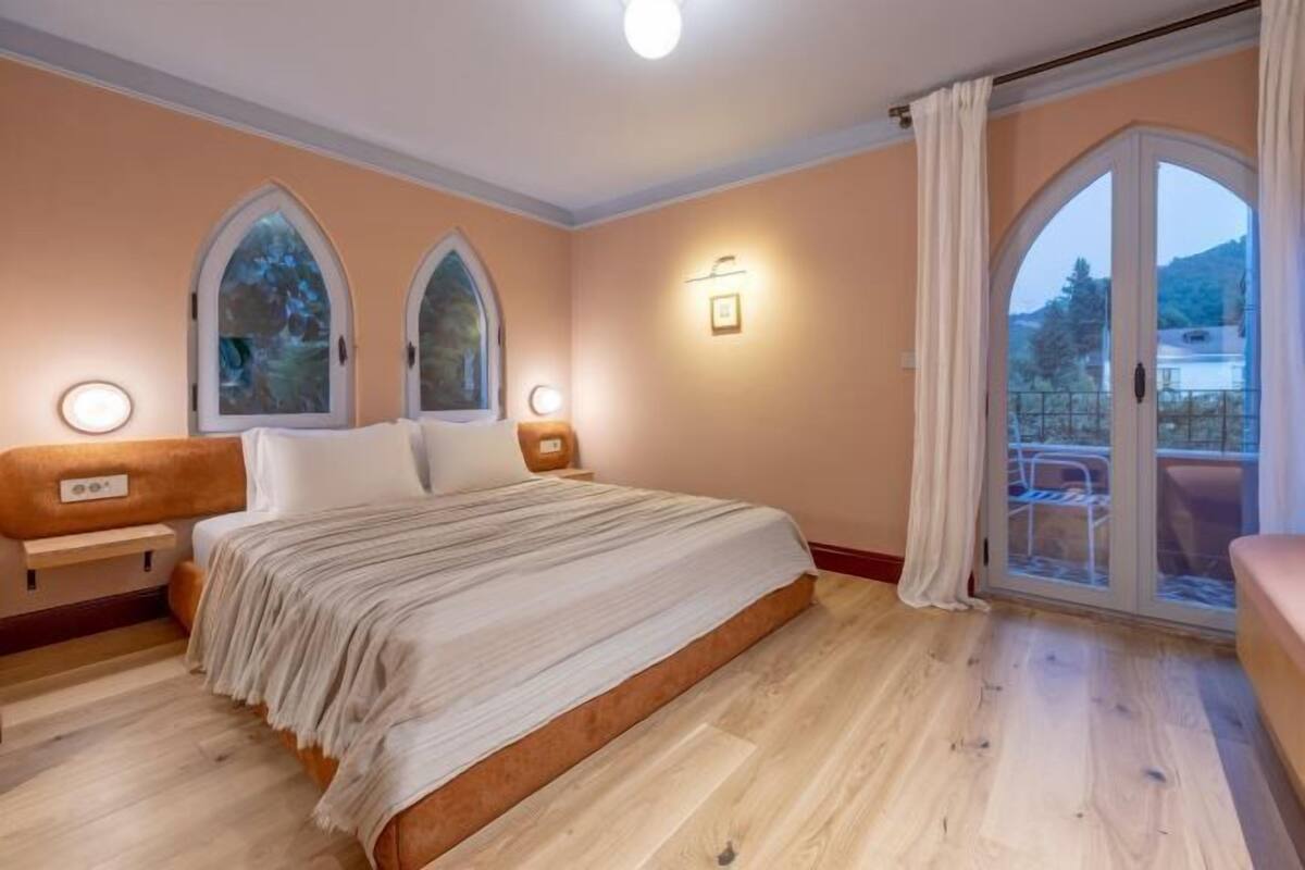 Une chambre avec un grand lit, deux lampes fixées au mur, une fenêtre avec des rideaux et une vue sur l’extérieur.