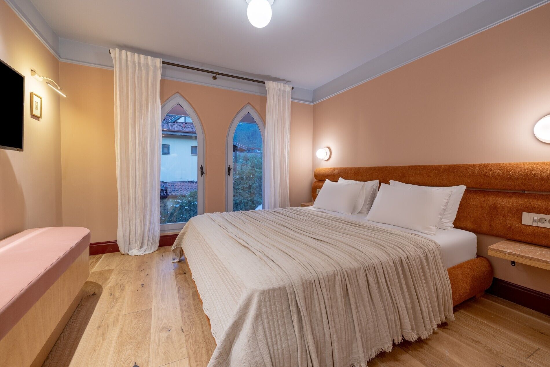 A bedroom with a bed, a bedside table, a TV, and a window with curtains.