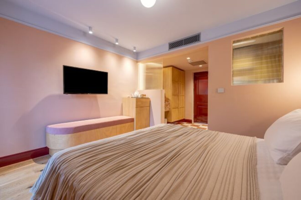 A bedroom with a bed, a flat-screen TV mounted on the wall, a bench, and a wardrobe.