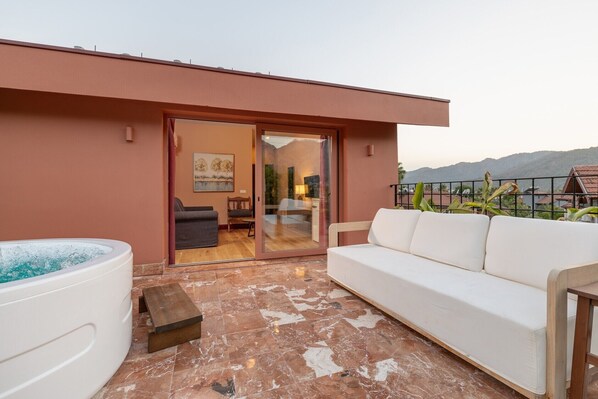 A modern outdoor living area with a white sofa, a hot tub, and a wooden bench. - Yonca Anjelika Otel (Fethiye)