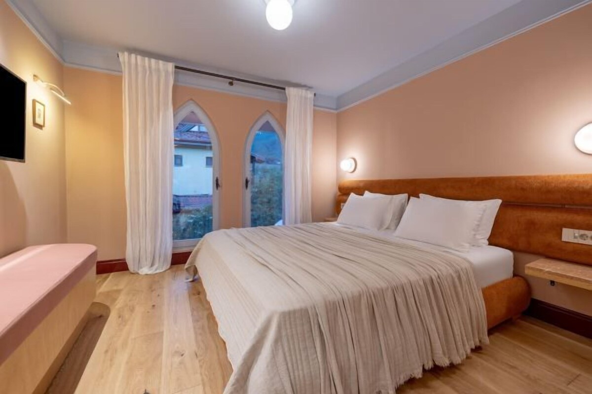 A bedroom with a bed, a bedside table, a TV, and a window with curtains.