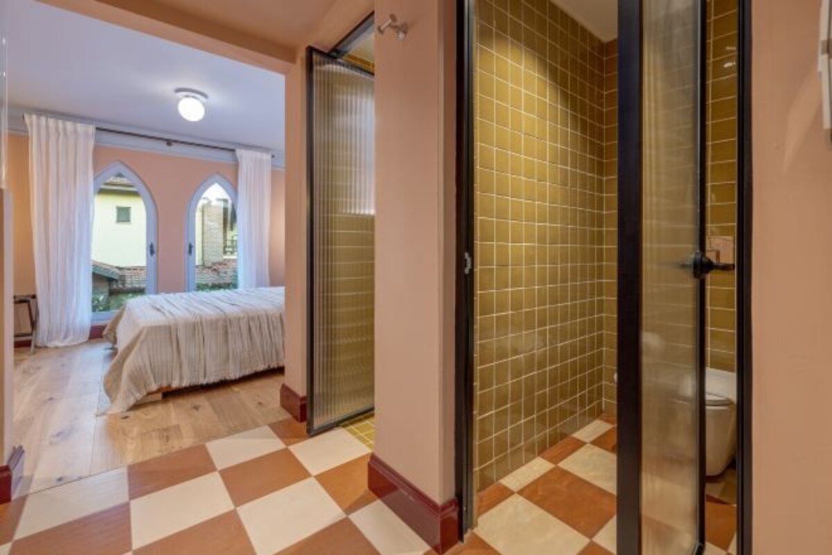 A bedroom with a checkered floor, a bed, and a bathroom with tiled walls.