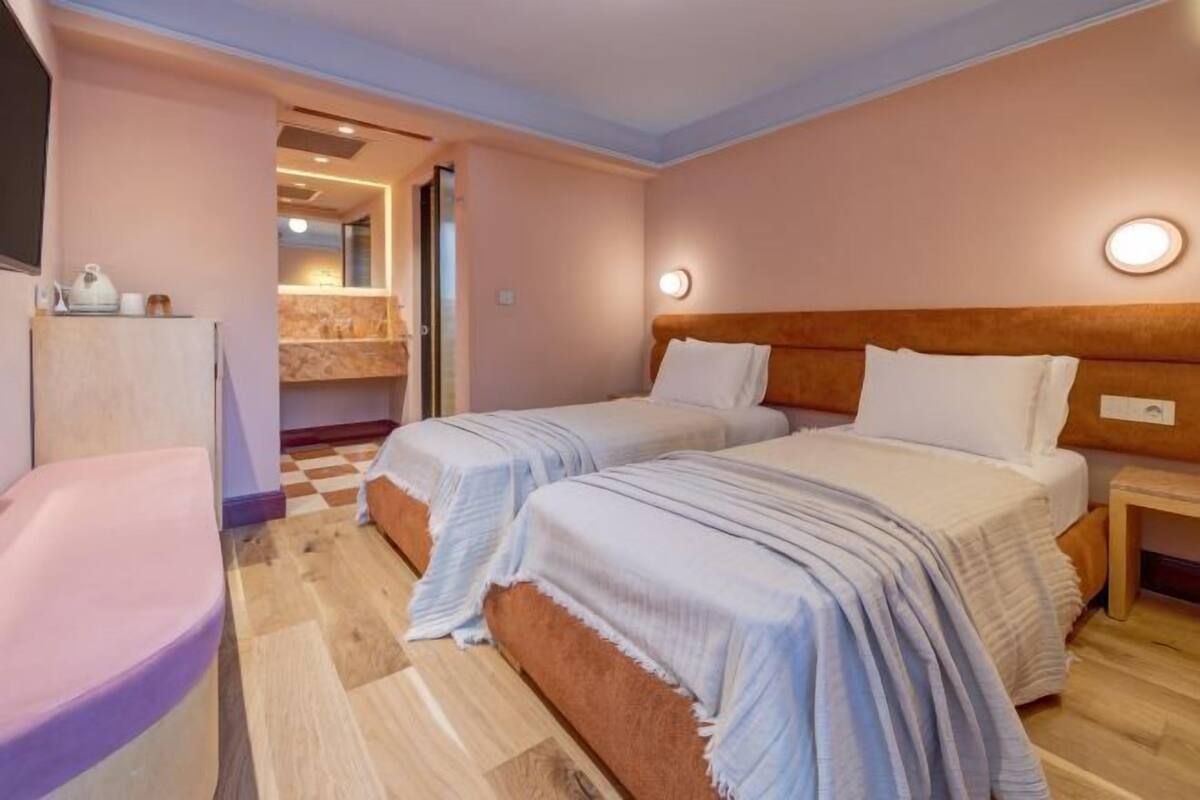 Une chambre d’hôtel avec deux lits, une petite table, une chaise et une salle de bain visible à travers une porte ouverte.