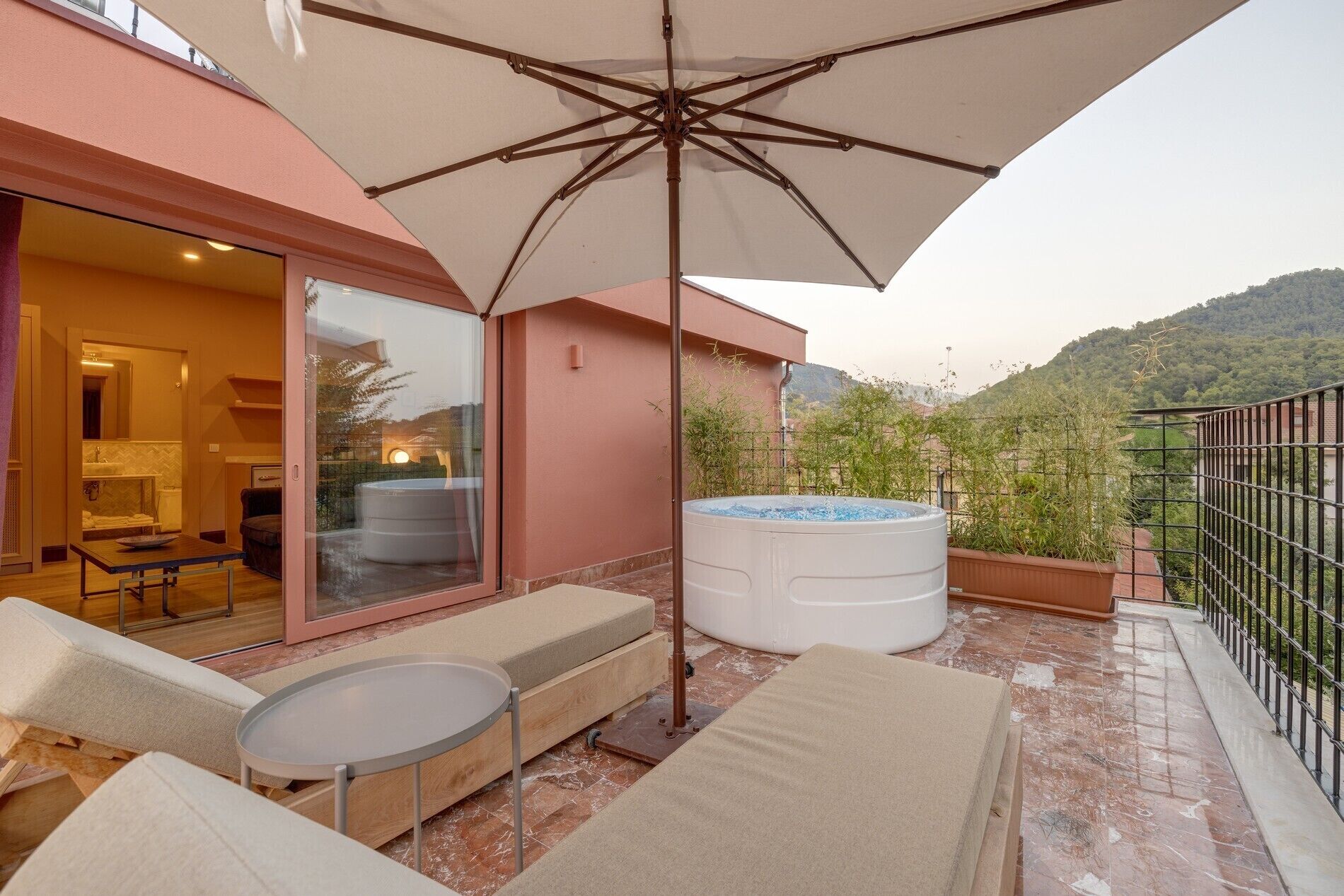 A balcony with a hot tub, outdoor seating, and a large umbrella.
