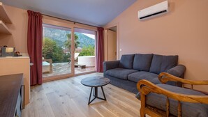 A modern living room with a grey sofa, wooden chairs, a small round table, and a sliding glass door leading to a balcony with a mountain view. - Yonca Anjelika Otel (Fethiye)
