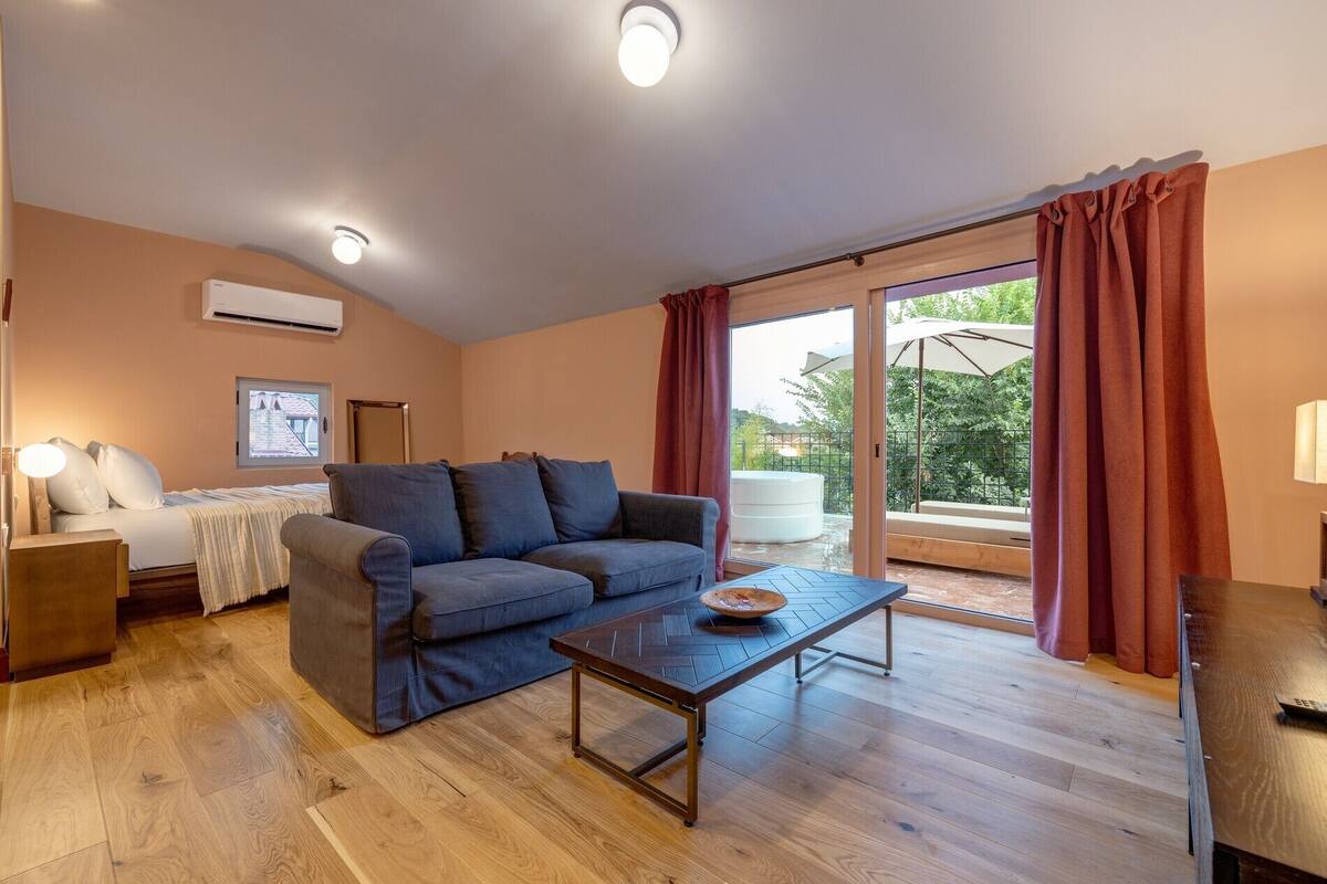 Un salon moderne avec un canapé, une table basse et un lit. Une porte-fenêtre coulissante donne accès à un espace extérieur doté d’un jacuzzi.