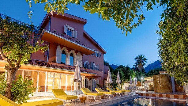 A two-story building with a pool, yellow lounge chairs, and umbrellas. - Yonca Anjelika Otel (Fethiye)