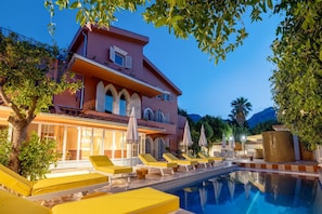 A two-story building with a pool, yellow lounge chairs, and umbrellas. - Yonca Anjelika Otel (Fethiye)