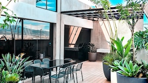 Un patio moderno al aire libre con zona de comedor, plantas en macetas grandes y vistas de la ciudad.