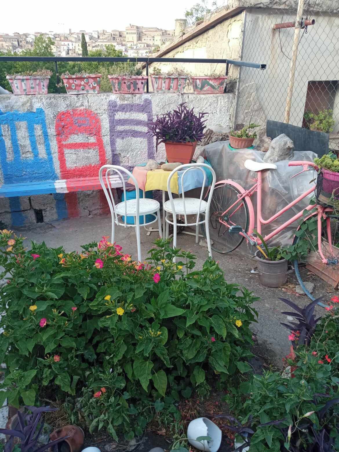 Un jardin sur le toit, avec une table et des chaises, un vélo rose et un banc orné de graffitis colorés.