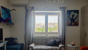 A living room with a sofa, a small table, a TV, and a window with curtains. -  Large ecohome a Tricarico near Matera, with kitchen,parking, green (Tricarico)