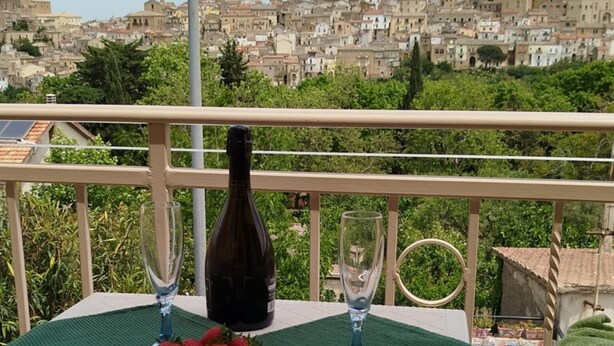A table with a bottle of wine, two glasses, and a bowl of strawberries on a balcony with a view of a densely packed town. -  Large ecohome a Tricarico near Matera, with kitchen,parking, green (Tricarico)