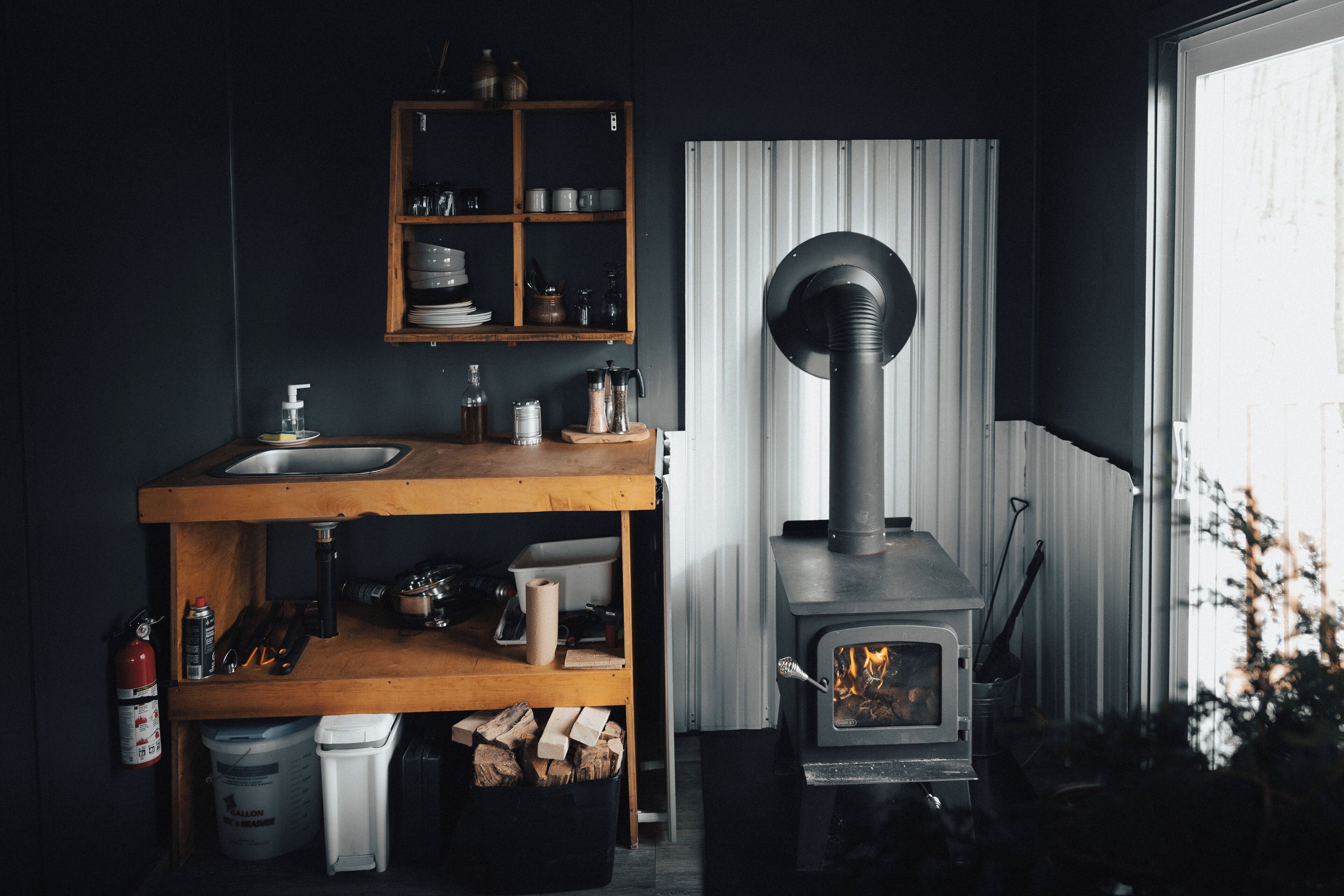 A kitchen with a wooden shelf, a sink, and a wood-burning stove.