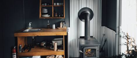 A kitchen with a wooden shelf, a sink, and a wood-burning stove.