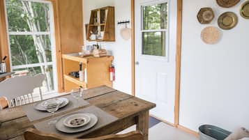 Una rústica mesa de madera dispuesta con platos y vasos, un armario de madera con utensilios de cocina, y una puerta blanca con un ventanal.