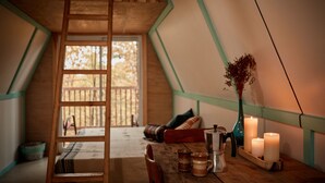 A cozy, triangular room with a wooden ladder, a table with candles, a vase with dried flowers, and a view of the outdoors through a window. - Station Chêne Rouge (Hatley)