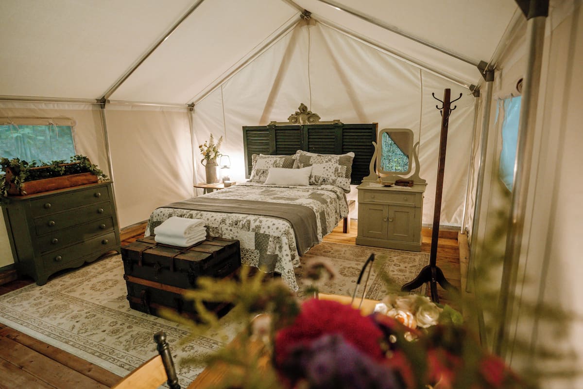 A tented room with a bed, dresser, lamp, and a window with a view.