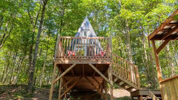 A wooden treehouse with a triangular roof and a wooden deck.