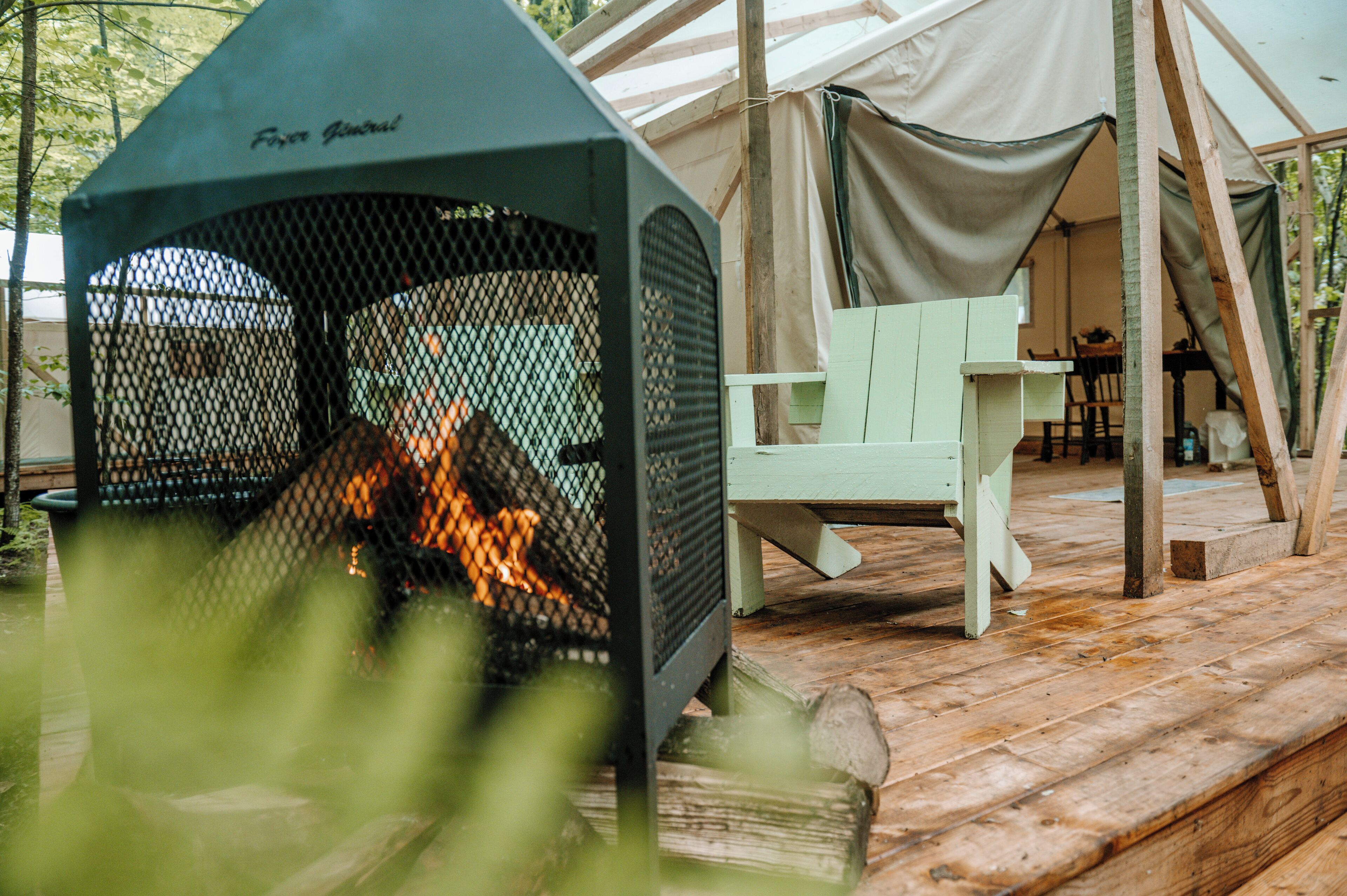 A tent with a fire pit in front, a wooden deck, and a green chair.