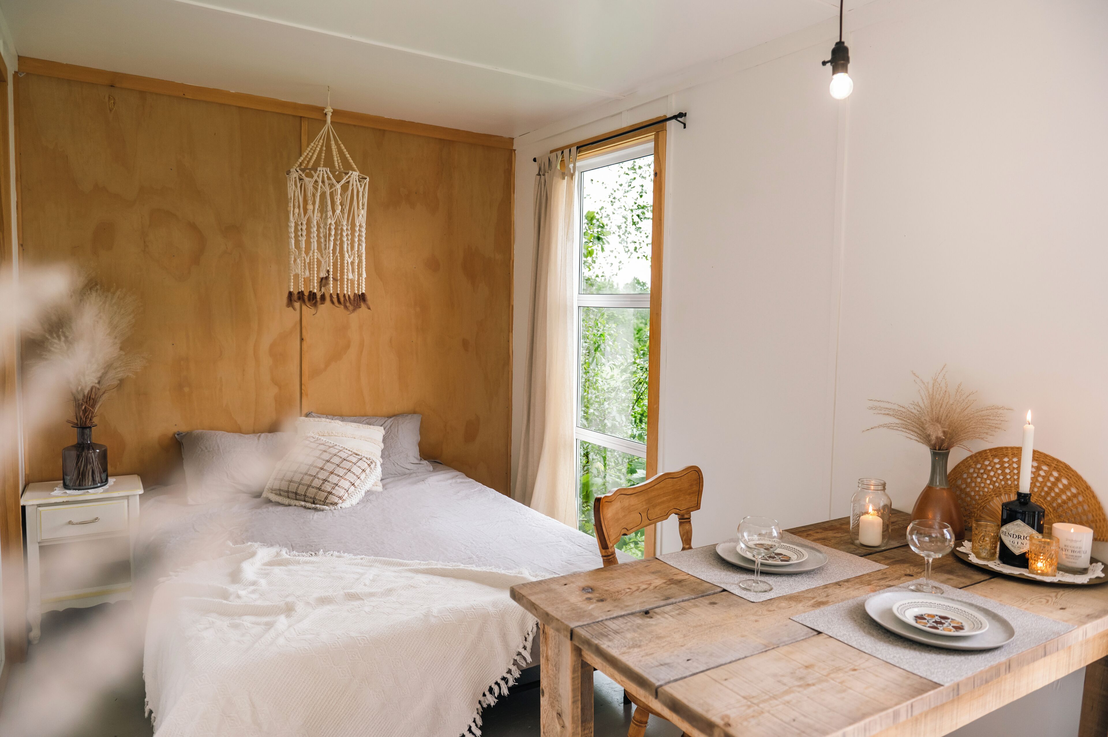 A bedroom with a wooden headboard, a bed with white bedding, a bedside table with a vase, and a window with curtains.