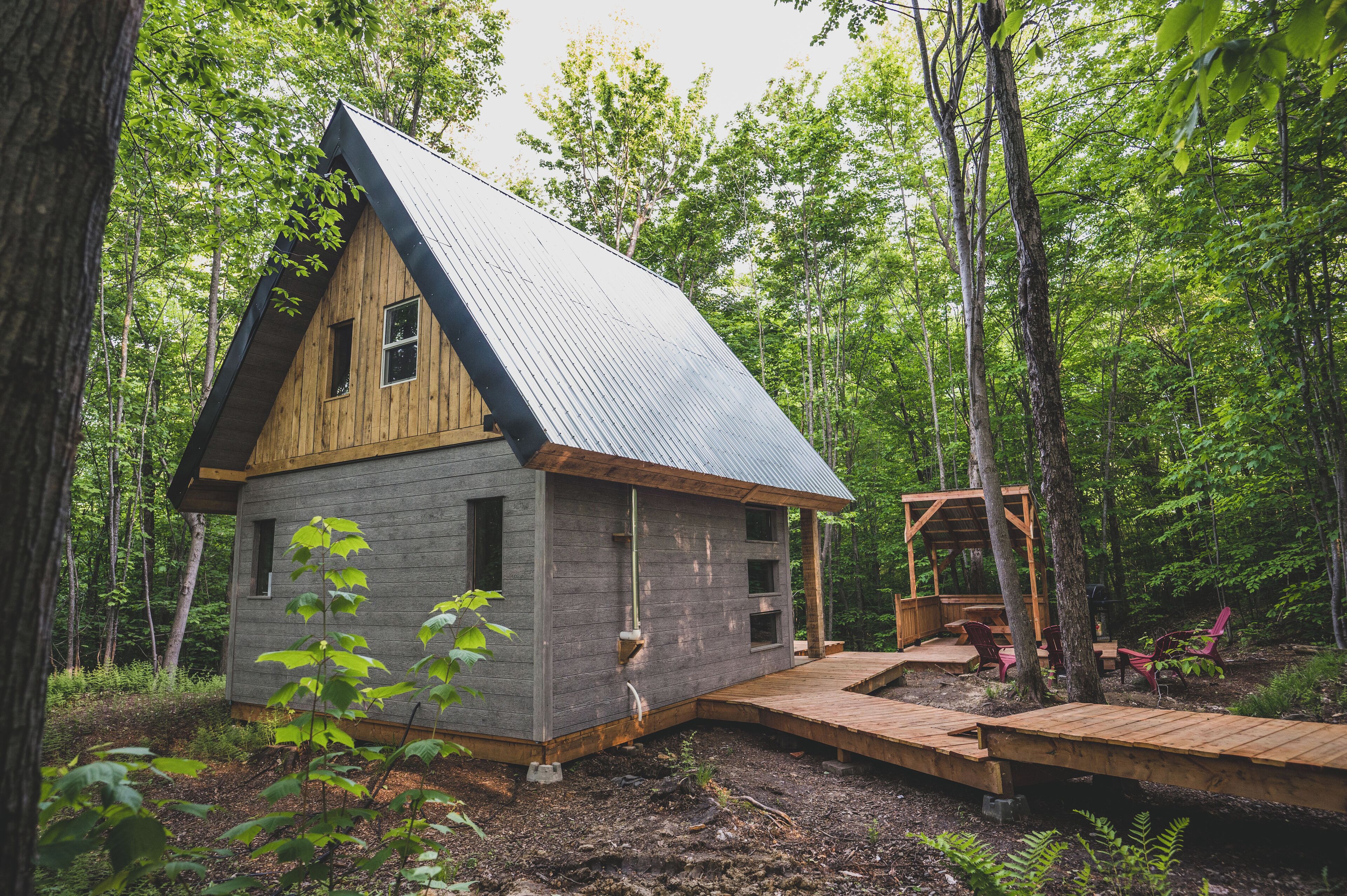 Une cabane rustique avec un toit en pente, un revêtement extérieur en bois et un petit porche doté de chaises.