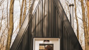 A person standing at a door of a building with a triangular roof, surrounded by trees. - Station Chêne Rouge (Hatley)