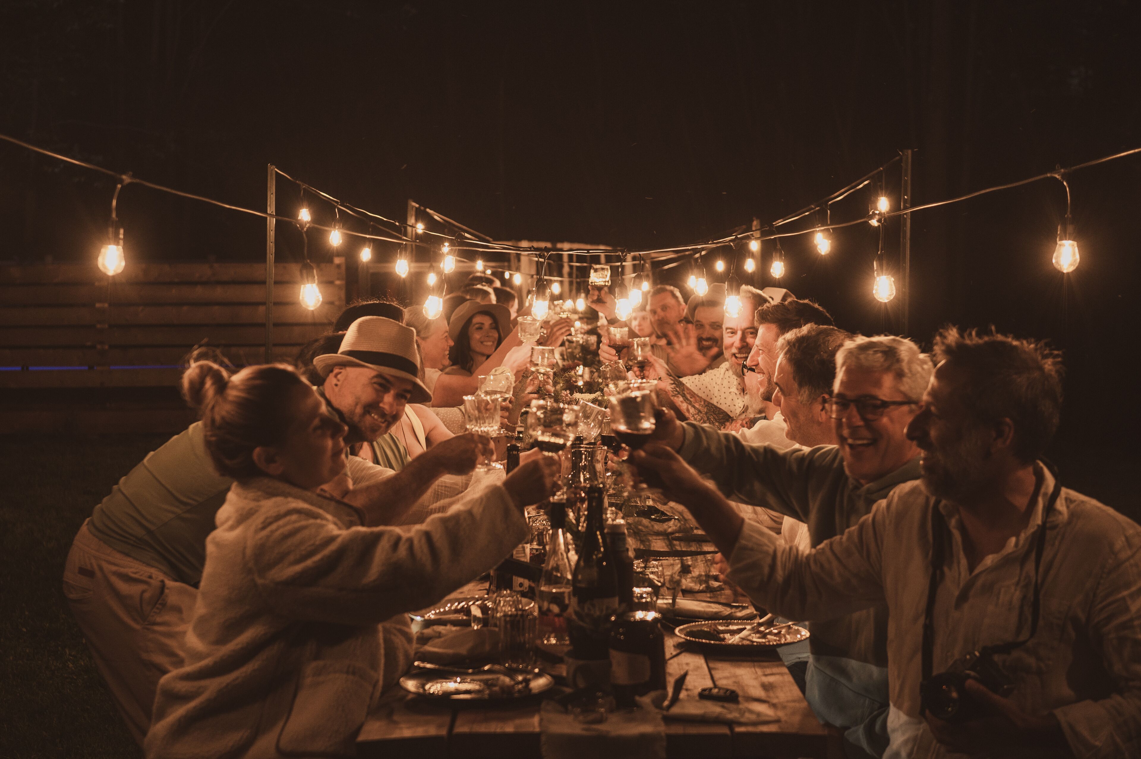 Un grupo de personas reunidas alrededor de una mesa, con luces de cuerda colgando del techo, participando en un evento social.