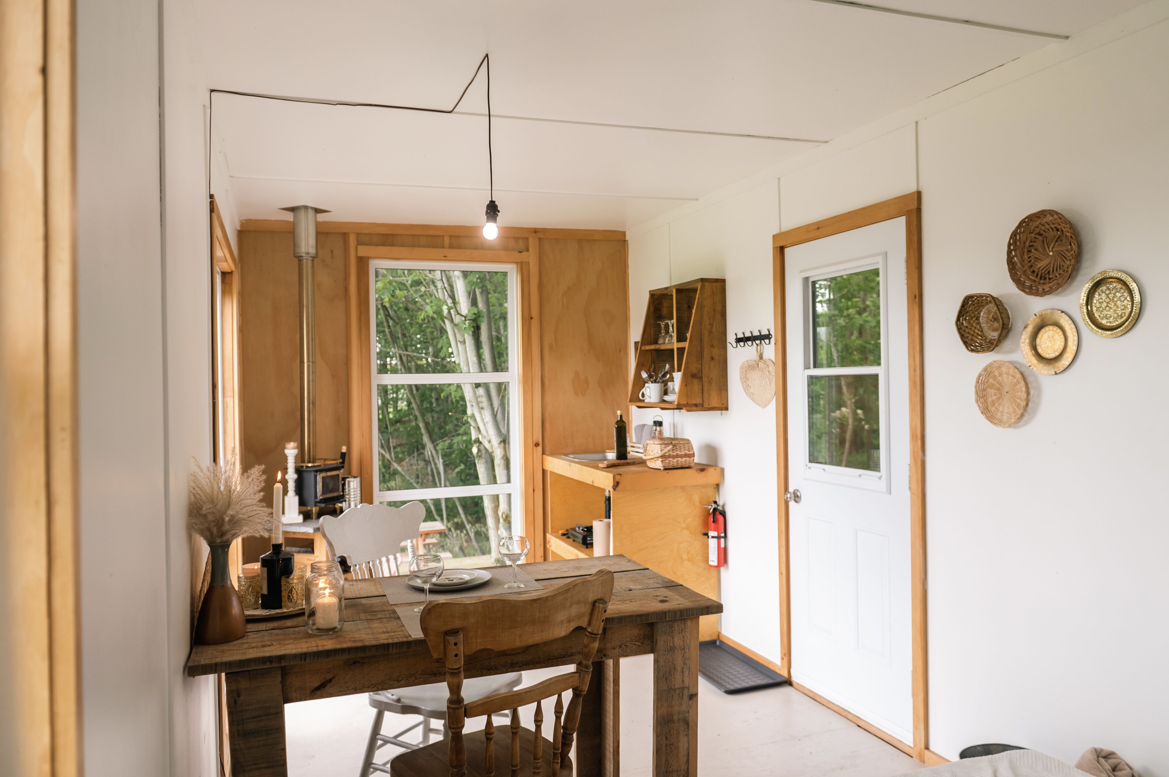 Una cocina compacta con una mesa y sillas de madera, una lámpara colgante y un ventanal con vistas a árboles.