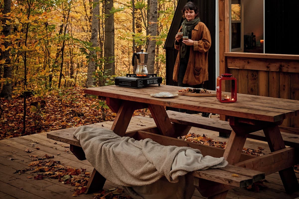 A wooden cabin with a picnic table and a person standing by the window.
