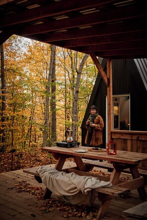 A wooden cabin with a picnic table and a person standing by the window. - Station Chêne Rouge (Hatley)