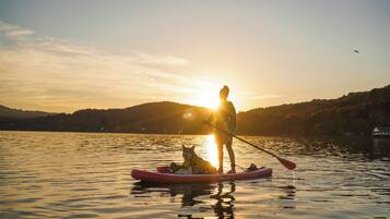 Uma pessoa e um cão em um caiaque vermelho em um lago calmo, com o sol se pondo ao fundo.