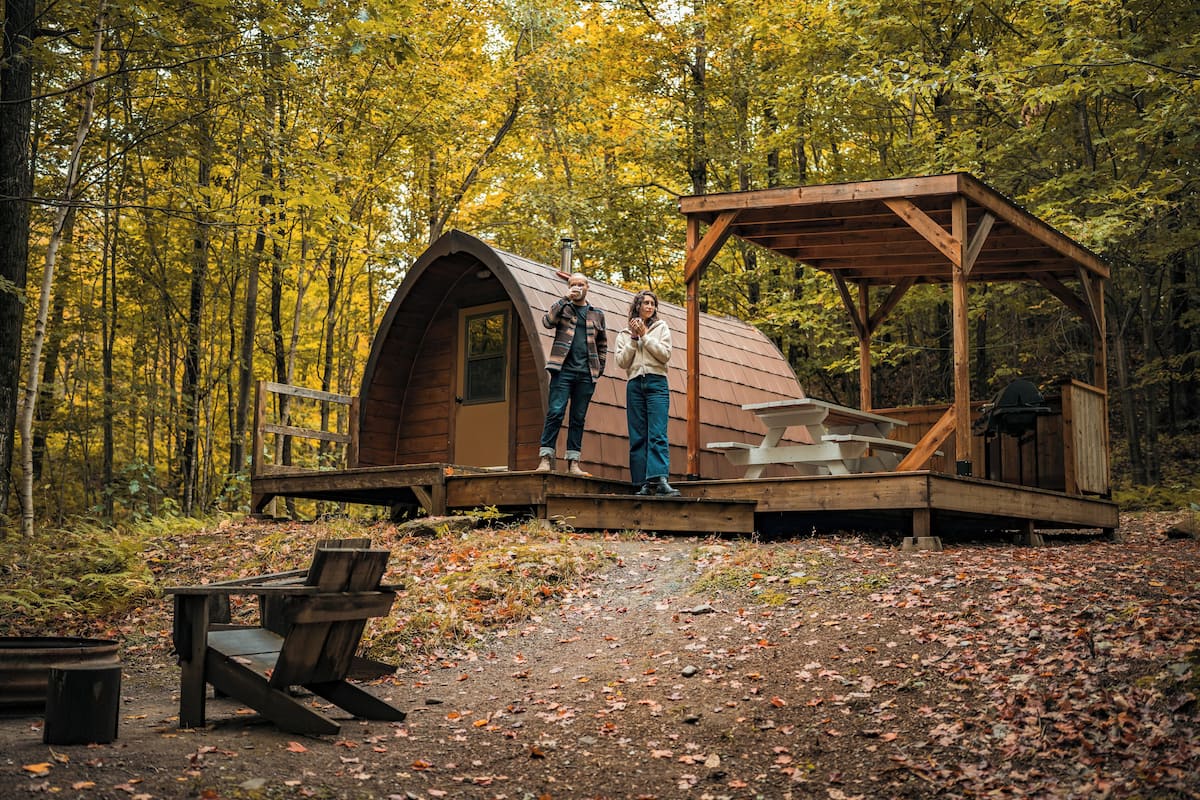 A rustic wooden cabin with a covered porch and a picnic table in a forested area.
